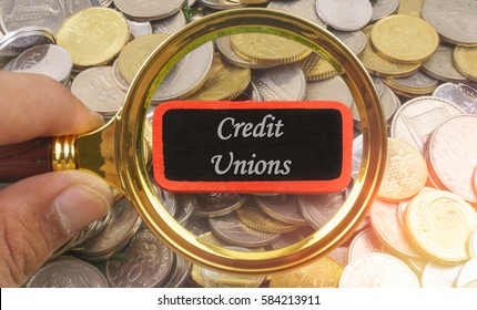 Man finger holding a magnifying glass with label written CREDIT UNIONS on gold and silver coins
