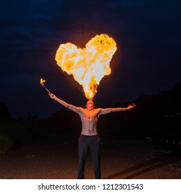 Man fire-eater blowing a large flamein the shape of a heart
 from his mouth at night - Powered by Shutterstock