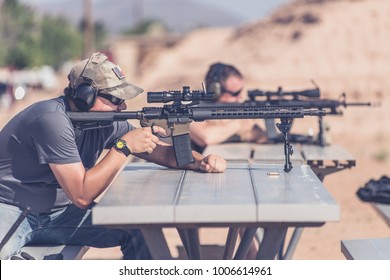 Man Firing Black Rifle On Desert Range Bench Rest With Bipod