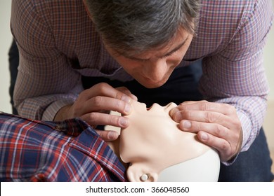 Man In First Aid Class Performing Mouth To Mouth Resuscitation On Dummy