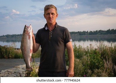 A Man With A Fish Caught In The Hands Of A Lake. Wild Pride.