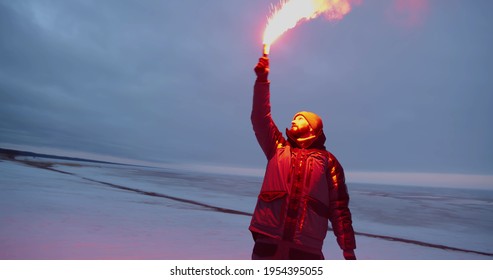 Man or fisherman firing red maritime distress signal flare on winter time. Portrait of male traveler lightening signal or firework torch standing on frozen lake
