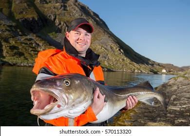 Man In A Fisherman's Cap Holding A Big Fish Cod. Smiling