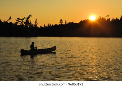 A Man Fishing From a Canoe at Sunset on a Remote Wilderness Lake - Powered by Shutterstock