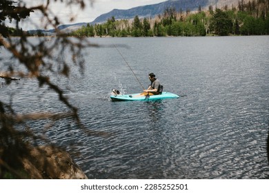 Man fishing in a kayak on a lake in mountains with dog - Powered by Shutterstock