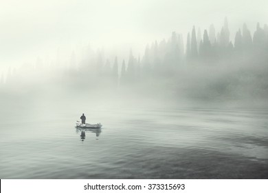 Man fishing on a boat in a mystic foggy lake