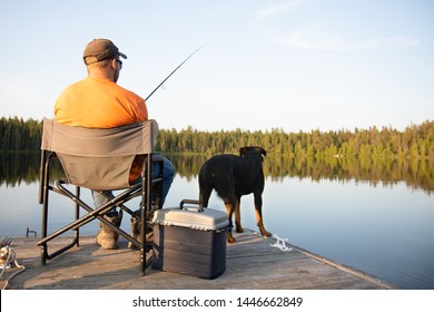 A man fishing outside at dusk on a lake in the summer on a wooden dock and a chair in Ontario Canada with his dog travel