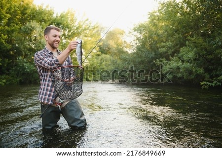 Man with fishing rod, fisherman men in river water outdoor. Catching trout fish in net. Summer fishing hobby.