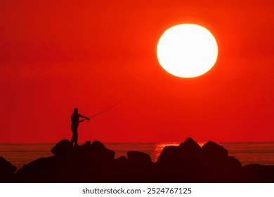 Man fishing with a fishing rod at sunset. Impressive image of red sky and sun. - Powered by Shutterstock