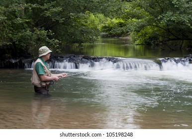 Man Fishing For Trout Next To A Small Waterfall