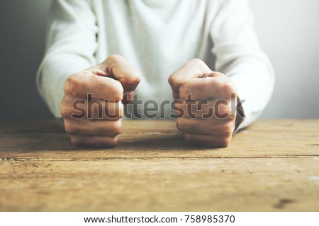 man fists clenched on a wooden table in anger