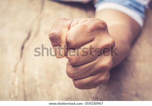 A man fists\
clenched on a wooden table in\
anger