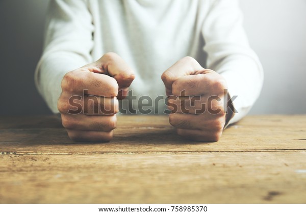 man fists\
clenched on a wooden table in\
anger