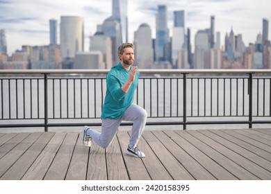 Man in fitness wear exercising near Manhattan. Healthy exercises. Active senior man is fitness exercising outdoor. Exercising after retirement. Senior man training legs muscles doing lunges exercise. - Powered by Shutterstock