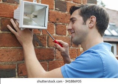 Man Fitting Security Light To House Wall