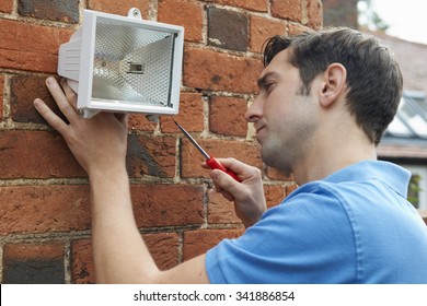 Man Fitting Security Light To Wall Of House