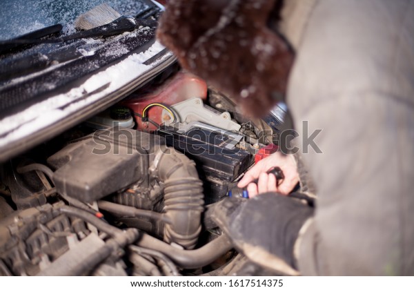A man fixing a car battery in a car.\
Accumulator discharged in cold winter,\
Russia