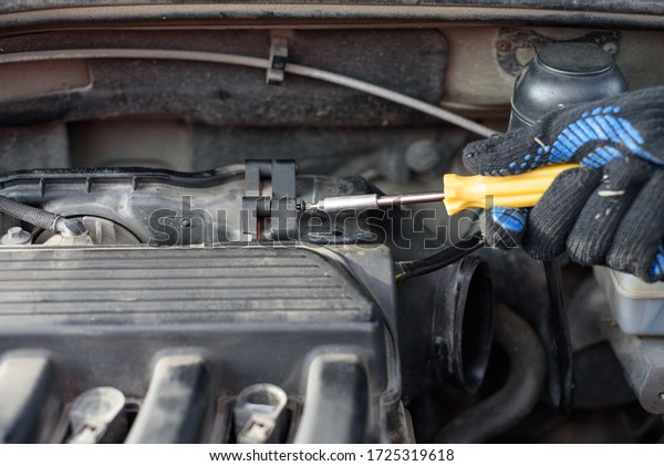 Man is fixing the car. Male hand unscrews an\
air filter in a car with a\
screwdriver
