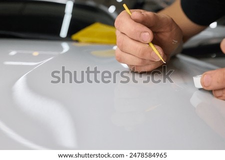 Man fixing car scratch precisely in repair shop, displaying craftsmanship in automotive maintenance