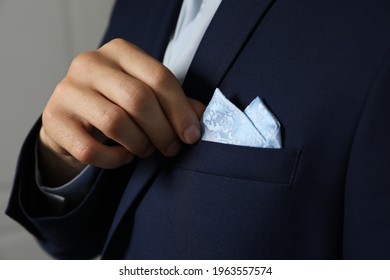 Man fixing handkerchief in breast pocket of his suit on light background, closeup