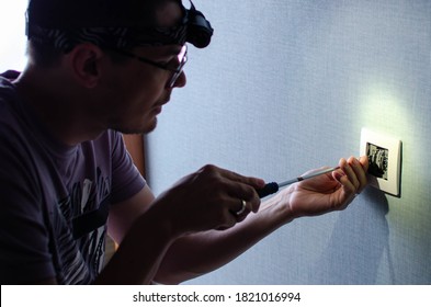 A Man With A Flashlight On His Head ?hanging Room Wall Light Switch Installation With A Screwdriver, Close-up Electrician Hands