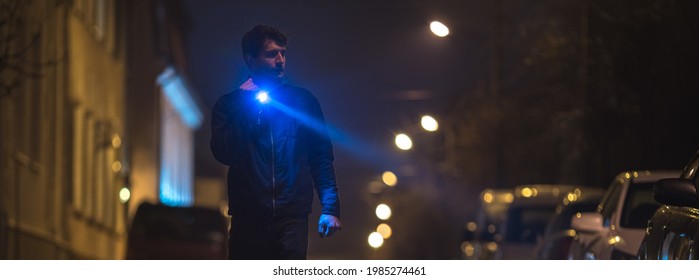 Der Mann mit einer Taschenlampe steht auf der nassen Straße. Abendnachtszeit