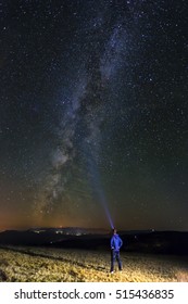 Man with a flashlight trying to light up the night sky and the milky way.