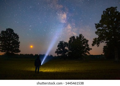 A man with a flashlight under the sky full of stars