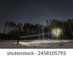 A man with a flashlight in a winter forest under the starry sky. 