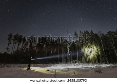 A man with a flashlight in a winter forest under the starry sky. 