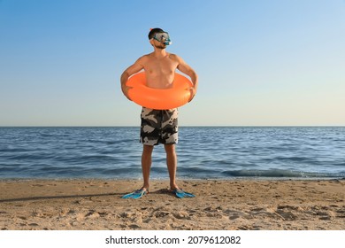 Man With Flippers, Inflatable Ring And Goggles On Sea Beach