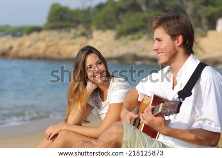 Man flirting playing guitar while a girl looks him amazed with the sea in the background