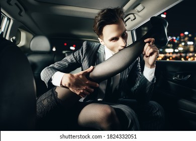 A Man Flirts With His Girlfriend Passionately Biting His Girlfriend's Leg In The Car. Love And Passion.