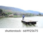 A man float on a raft on the river beside hill
