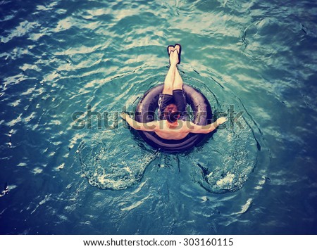a man floating down a river in a blow up tube with a baseball cap on and shorts on a hot summer day from overhead toned with a retro vintage instagram filter effect