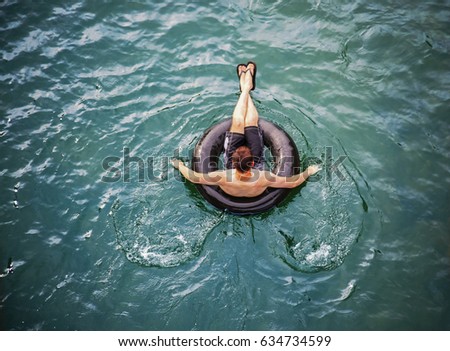 a man floating down a river in a blow up tube with a baseball cap on and shorts on a hot summer day from overhead