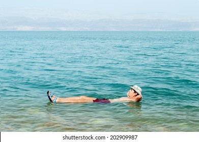 Man Floating In A Glassy Water Of Dead Sea With Outstretched Arms 