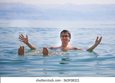 Man Floating In A Glassy Water Of Dead Sea With Arms Under His Forehead 
 