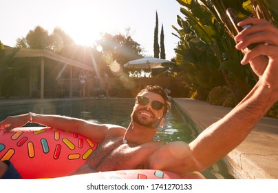 Man Floating On Inflatable Ring At Summer Pool Party Taking Selfie On Mobile Phone