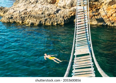 Man Floating In Sea Water On Back. Bay With Rocky Beach And Suspension Bridge. Copy Space. Summer Vacation