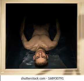 Man floating in a sensory deprivation isolation tank filled with dense salt water used in meditation, therapy, and alternative medicine. The boarders of the tank gives context.