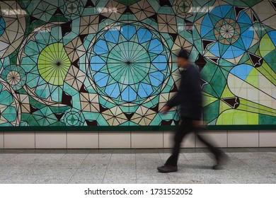 A man with a flu image walking in front of the wall consisting of a blue and green colored circular ceramic plate taken with long exposure