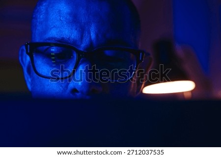 Man focused on computer screen with blue light reflecting on his face and glasses