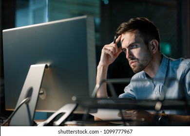 Man focusing on information in computer working alone late at night in modern office. 