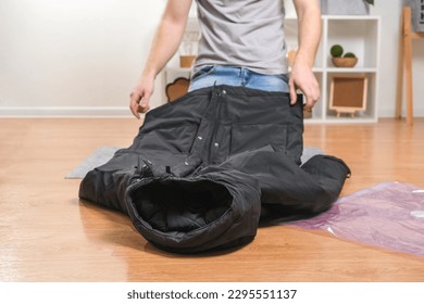 Un hombre dobla las chaquetas de invierno y las pone en una bolsa de vacío para almacenarlas en el armario durante la temporada. Ahorro de espacio y cuidadoso almacenamiento de ropa. Organización del almacenamiento.