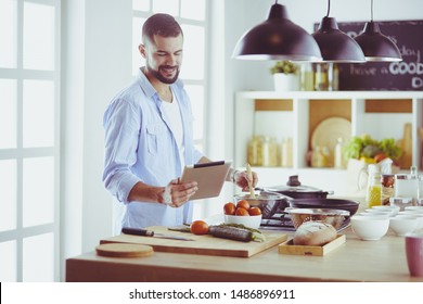 Man Following Recipe On Digital Tablet And Cooking Tasty And Healthy Food In Kitchen At Home