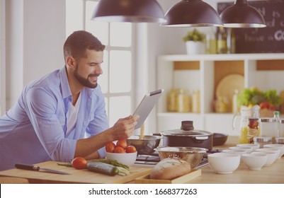 Man following recipe on digital tablet and cooking tasty and healthy food in kitchen at home - Shutterstock ID 1668377263