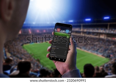 Man at a football match follows the odds and the current score. The concept of online sports betting. Football stadium and crowd in the background