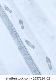 Man Footprint And Car Wheel Track On White Winter Snow. Track In Snow. Flat Lay / Overhead View. Snowy Road. Winter Footsteps Background.