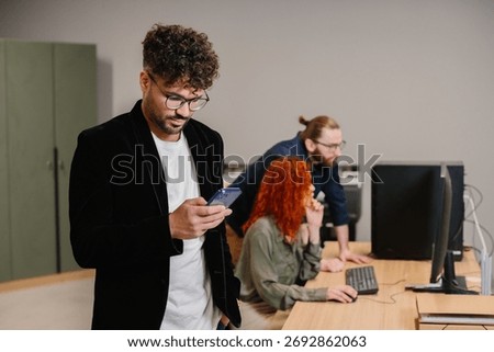 Man in foreground using mobile device while coworkers collaborate on computer project in modern office setting